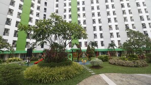 A residential building with a green and white facade, multiple balconies, and a playground area with slides and swings. - RedLiving Apartemen Green Lake View Ciputat - Pelangi Rooms Tower E (South Tangerang)