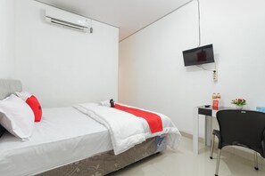 A hotel room with a bed, a desk, a chair, a TV, and a small table with a vase of flowers. - RedDoorz near RSU Suaka Insan (Banjarmasin)