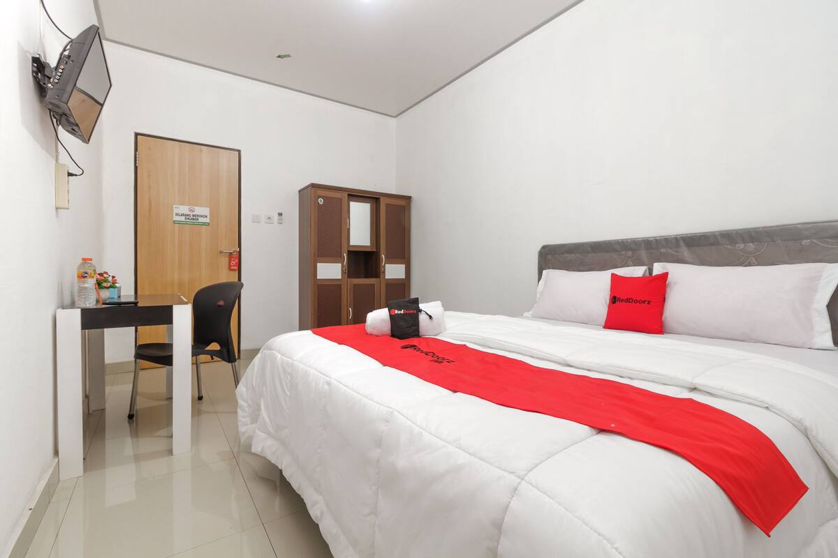 A hotel room with a bed, a desk, a chair, a wardrobe, and a television mounted on the wall.