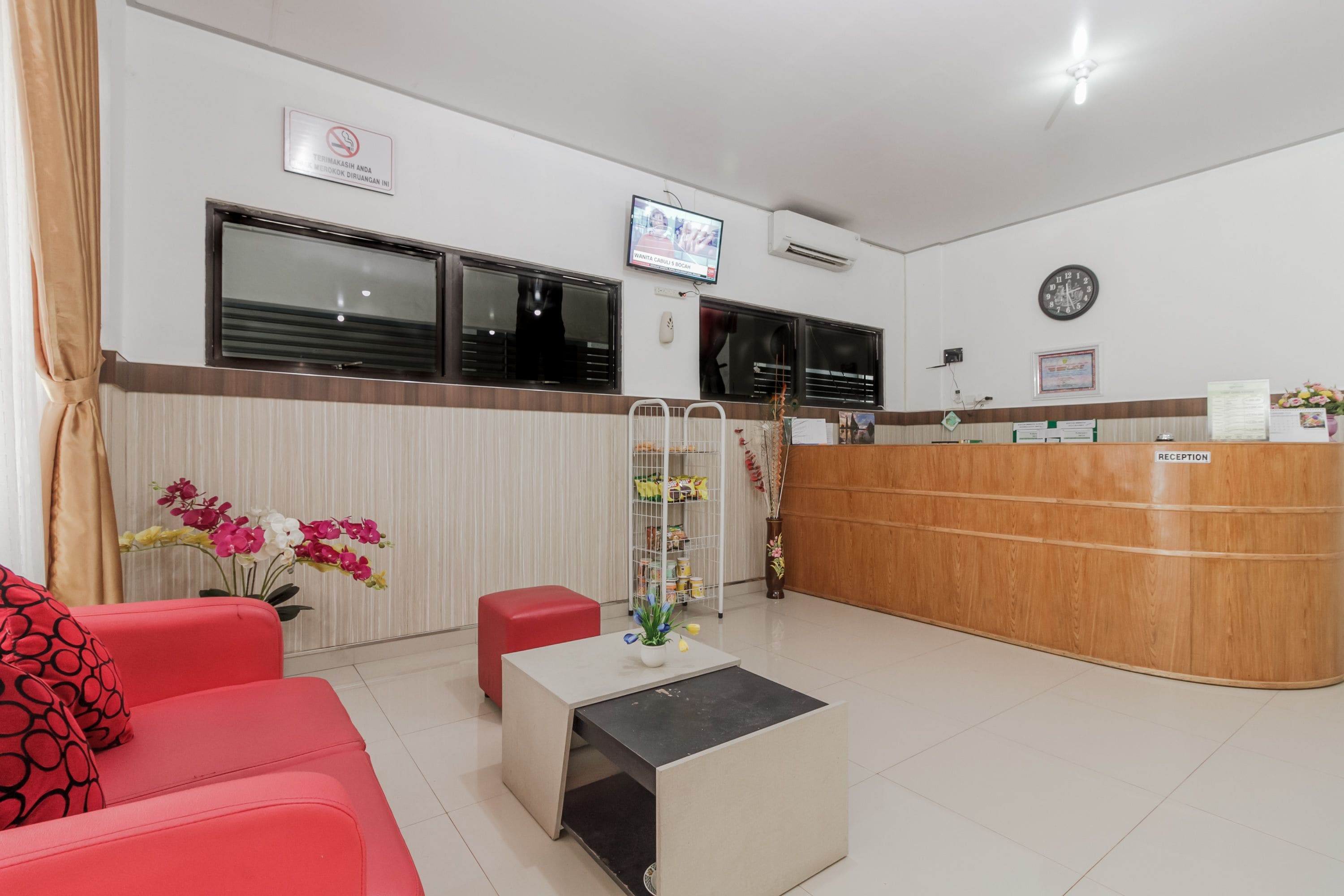 A reception area with a wooden desk, a TV mounted on the wall, a clock, and a sign indicating a smoking area.