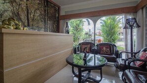 A modern hotel lobby with a wooden reception desk, leather seating, a glass coffee table, and a large mural of trees. - RedDoorz Syariah Plus @ Banjarbaru (Banjarbaru)