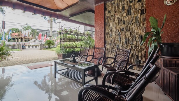 A spacious outdoor seating area with a stone wall, a wooden table, and wicker chairs. - RedDoorz Syariah Plus @ Banjarbaru (Banjarbaru)