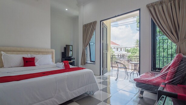 A hotel room with a bed, a TV, a balcony with a table and chairs, and a view of the outside. - RedDoorz near Sultan Thaha Airport Jambi (Jambi)