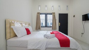 A hotel room with a bed, a TV, and a window with curtains. - RedDoorz near Sultan Thaha Airport Jambi (Jambi)