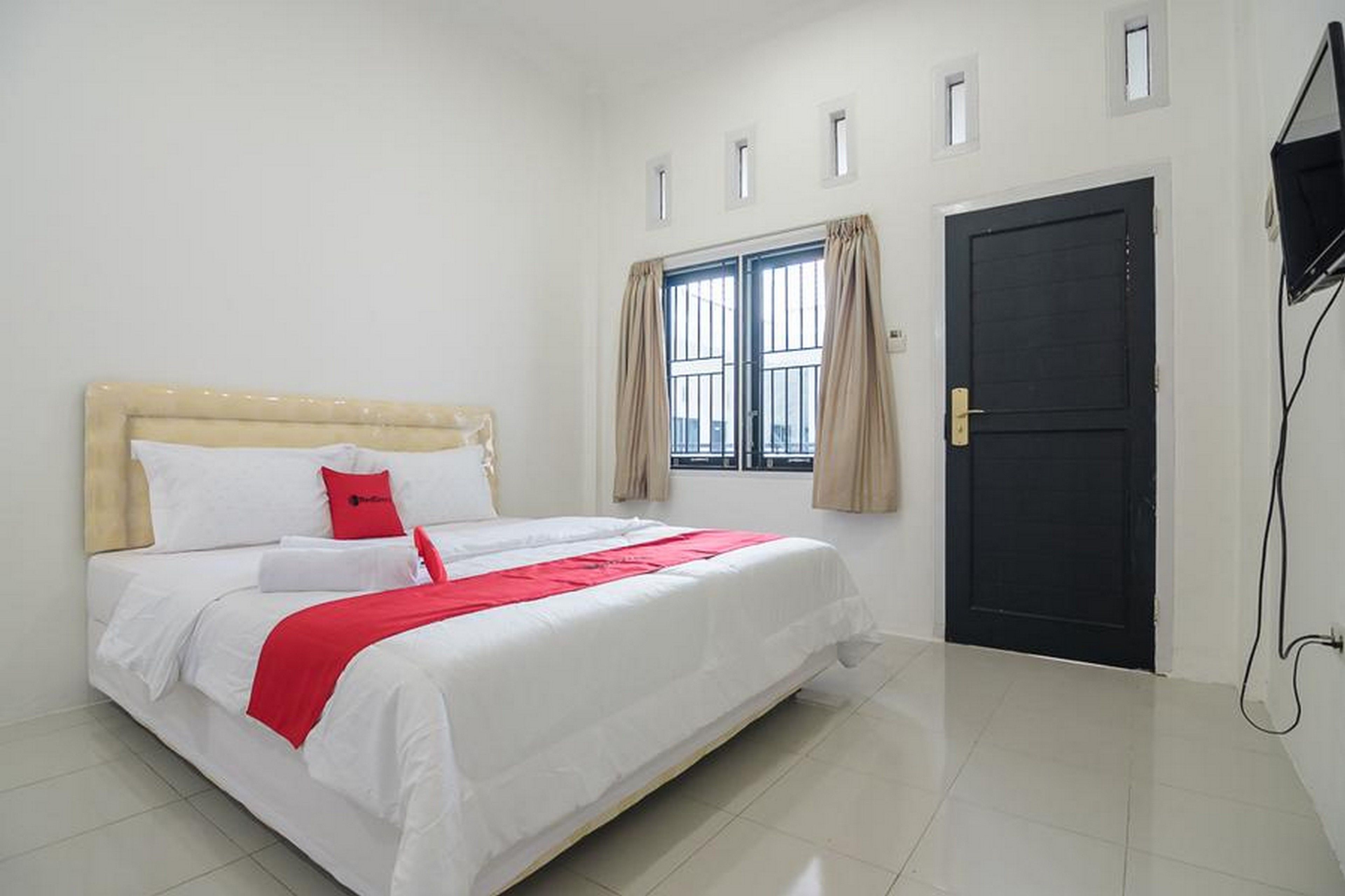 Habitación de hotel con cama, ventana con cortinas, puerta y televisor montado en la pared.