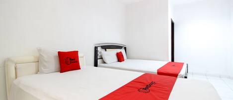 A hotel room with two beds, each with a red and white bedspread, and a white headboard.