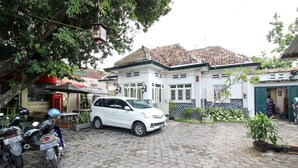 A white car parked on a cobblestone driveway in front of a building with a tiled roof and a green door. - RedDoorz Syariah near Wijilan Yogyakarta (Yogyakarta)