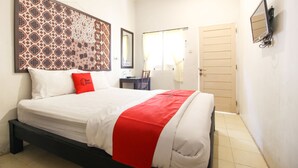 A hotel room with a bed, a red throw, a large patterned tapestry, a mirror, a TV, and a door. - RedDoorz Syariah near Wijilan Yogyakarta (Yogyakarta)