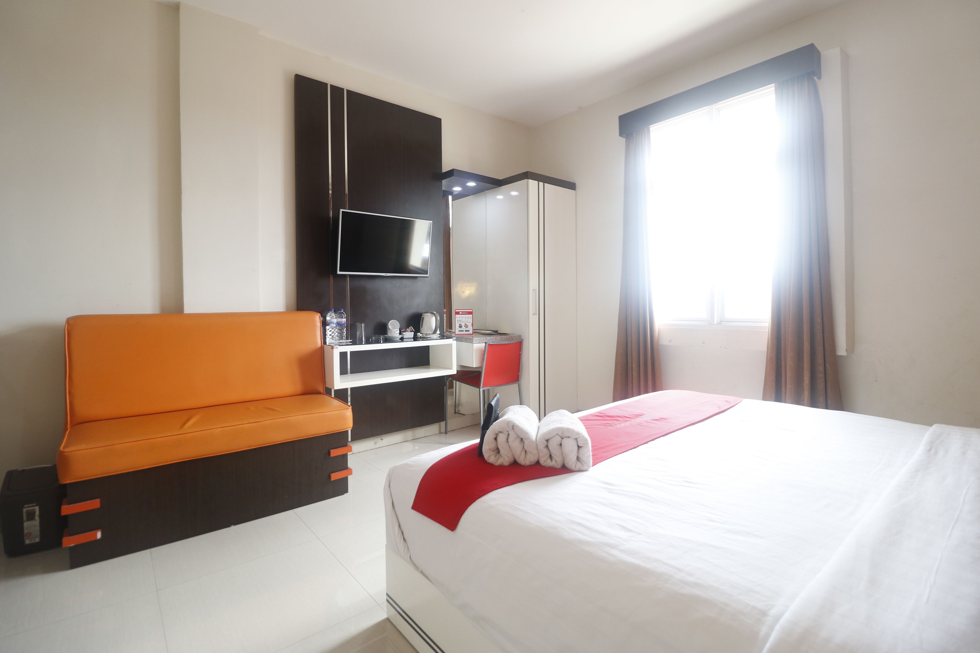 Ein Hotelzimmer mit Bett, Sofa, Schreibtisch, Fernseher und einem Fenster mit Vorhängen.