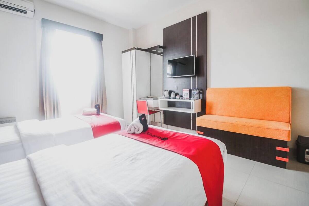 A hotel room with two beds, a desk with a chair, a TV, and a wardrobe.