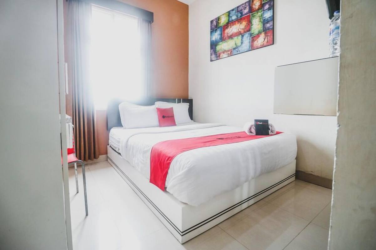 A modern hotel room with a bed, a chair, a window with curtains, and a colorful artwork on the wall.