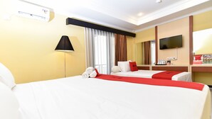 Ein Hotelzimmer mit zwei Betten, einem Fernseher, einem Schreibtisch mit Computer und einem Fenster mit Vorhängen.