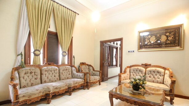 A traditional living room with two ornate sofas, a glass coffee table, and a large framed artwork on the wall. - RedDoorz Plus @ Tegal Panggung (Yogyakarta)
