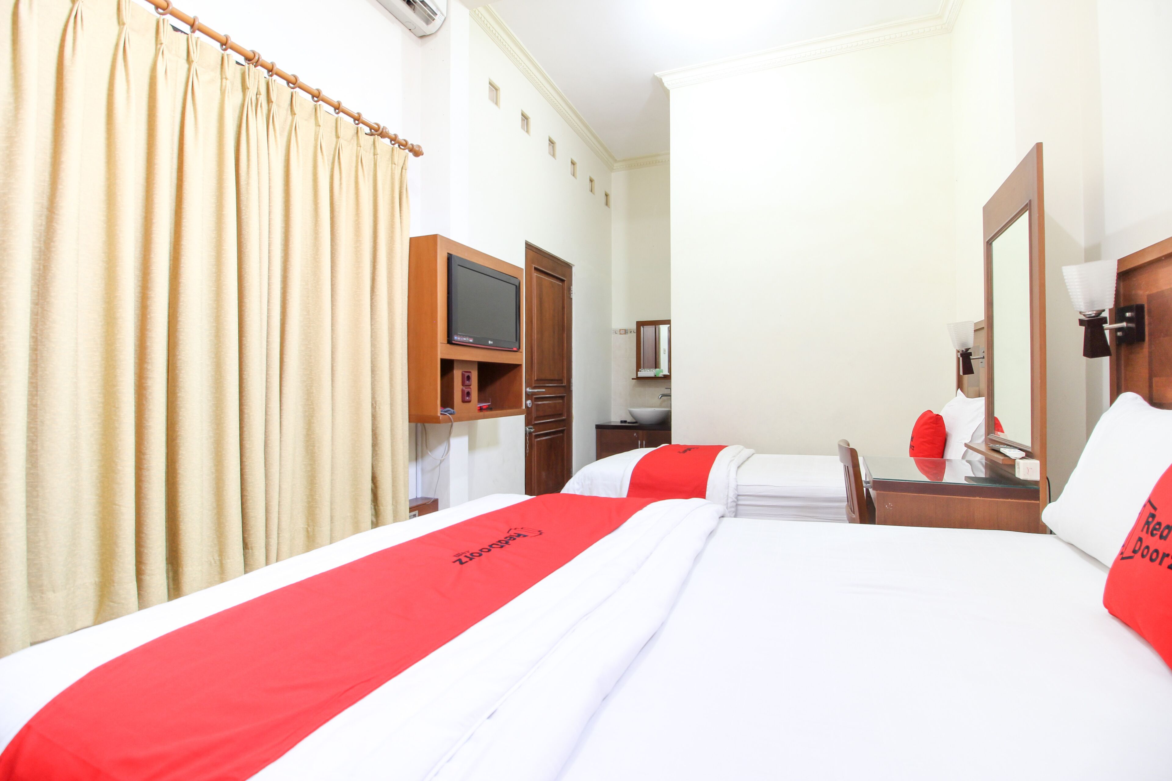 A hotel room with two beds, a TV, a desk, and a mirror.