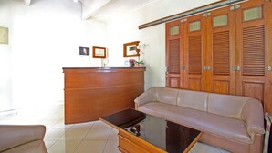 A reception area with a wooden desk, a sofa, and a glass-top coffee table. - RedDoorz Plus @ Tegal Panggung (Yogyakarta)