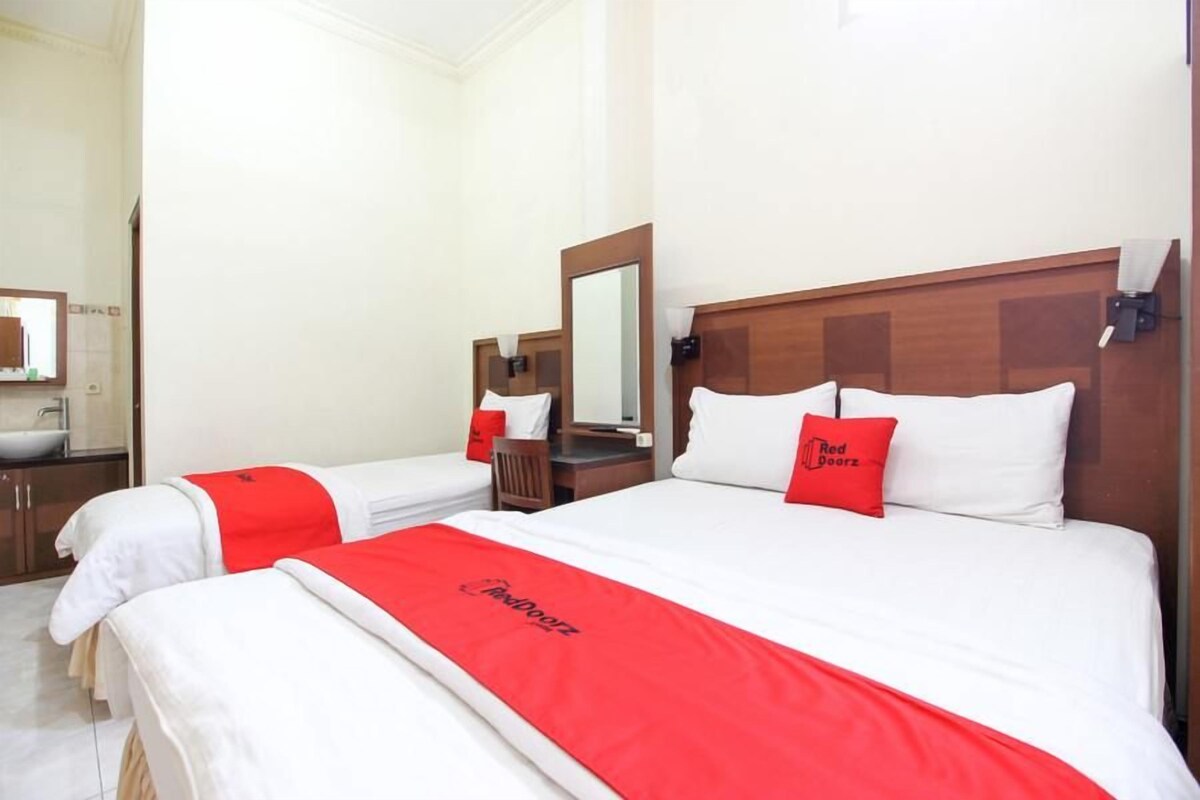 A hotel room with two beds, each with a red and white bedspread, a wooden headboard, and a mirror above the bed.
