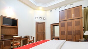 A hotel room with a bed, a desk with a chair, a television mounted on the wall, and a wardrobe. - RedDoorz Plus @ Tegal Panggung (Yogyakarta)