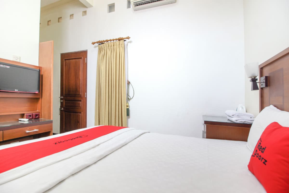 A hotel room with a bed, a television on a wooden dresser, a curtain, and a wall-mounted air conditioning unit.