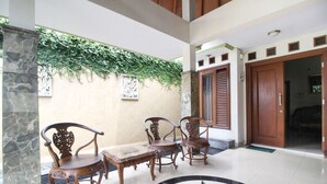 A lobby with a tiled floor, a wooden bench, two chairs, a stone pillar, and a wall with greenery. - RedDoorz Plus @ Tegal Panggung (Yogyakarta)