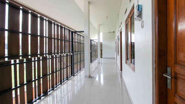 A corridor with a metal fence on one side, a wooden door on the other, and a clean, tiled floor. - RedDoorz Syariah @ Griya Izzara Guest House (Yogyakarta)