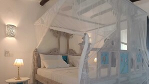 A bedroom with a canopy bed, a bedside table with a lamp, and artwork on the walls. - Pole Pole Beach House (Watamu)