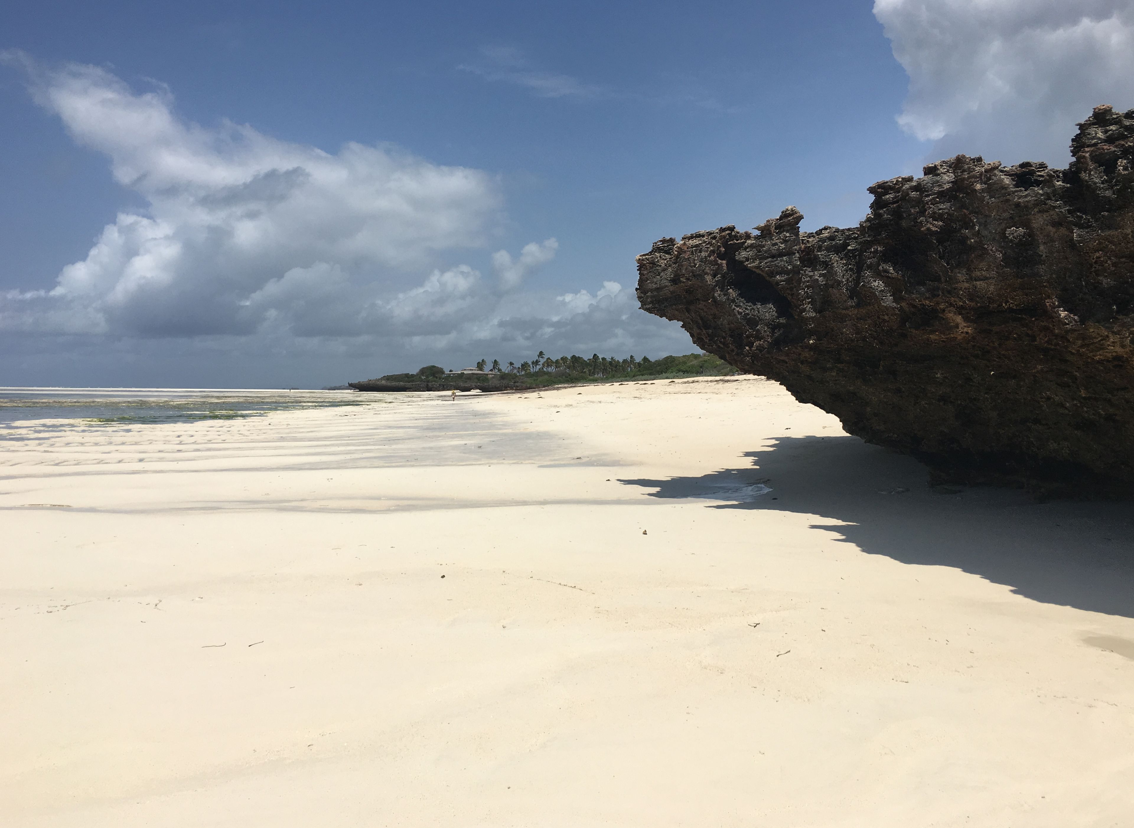 A beach with white sand, a rocky cliff, and a clear sky.