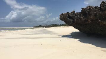 A beach with white sand, a rocky cliff, and a clear sky.