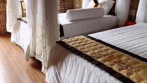 Een slaapkamer met een hemelbed, houten vloeren en een wand van bamboe.