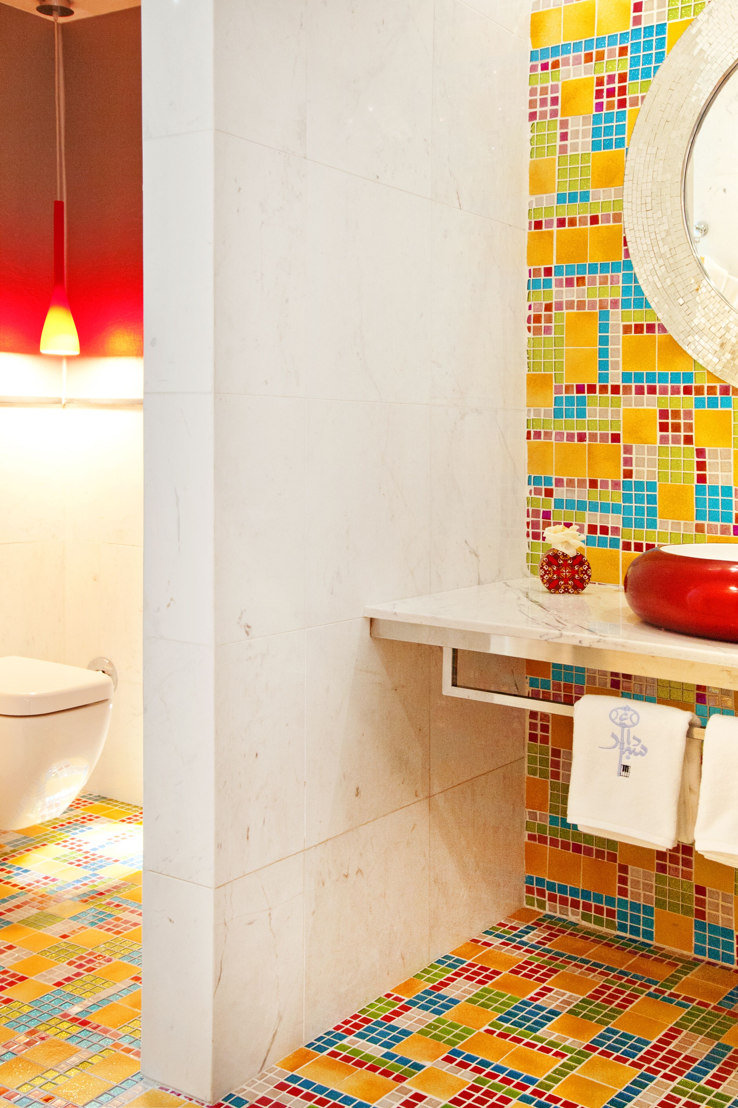A bathroom with a colorful mosaic tile floor, a white toilet, and a red basin on a white countertop.