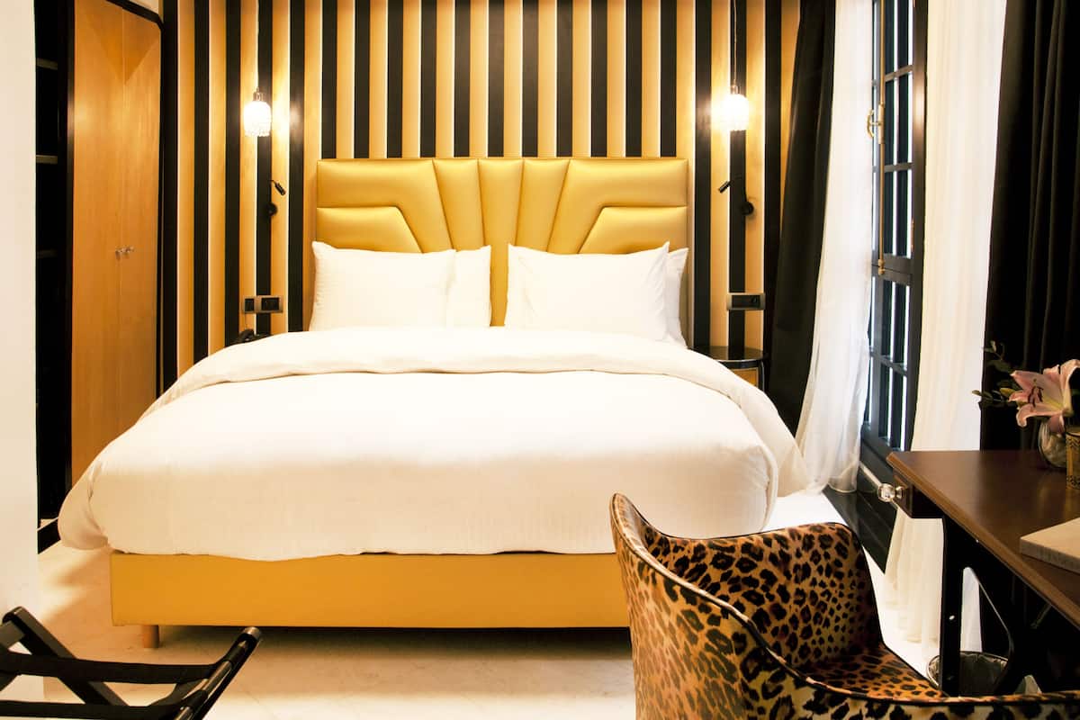A hotel room with a large bed, a headboard with vertical stripes, a leopard print chair, and a small table with a vase of flowers.