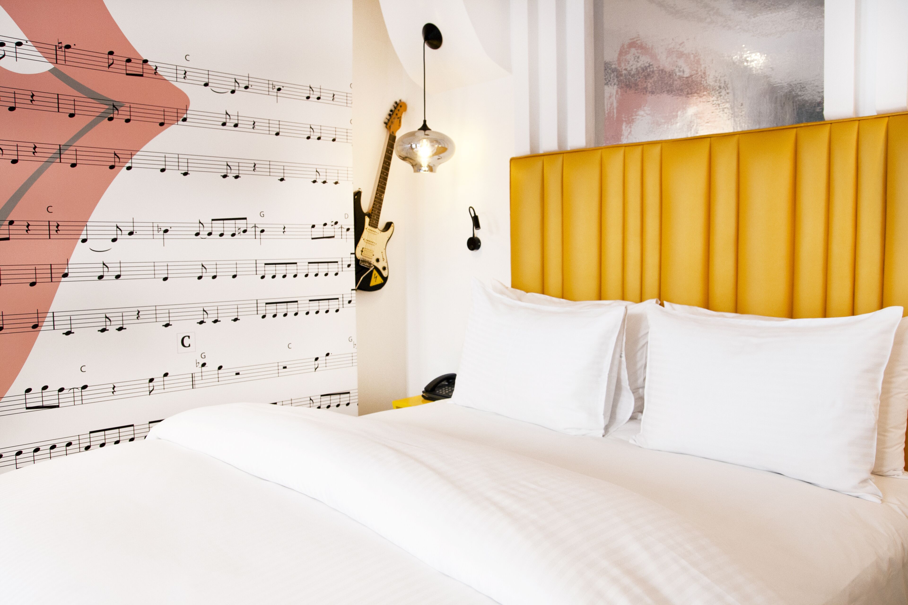 Habitación de hotel con una cama, una guitarra y una pared decorada con notas musicales.