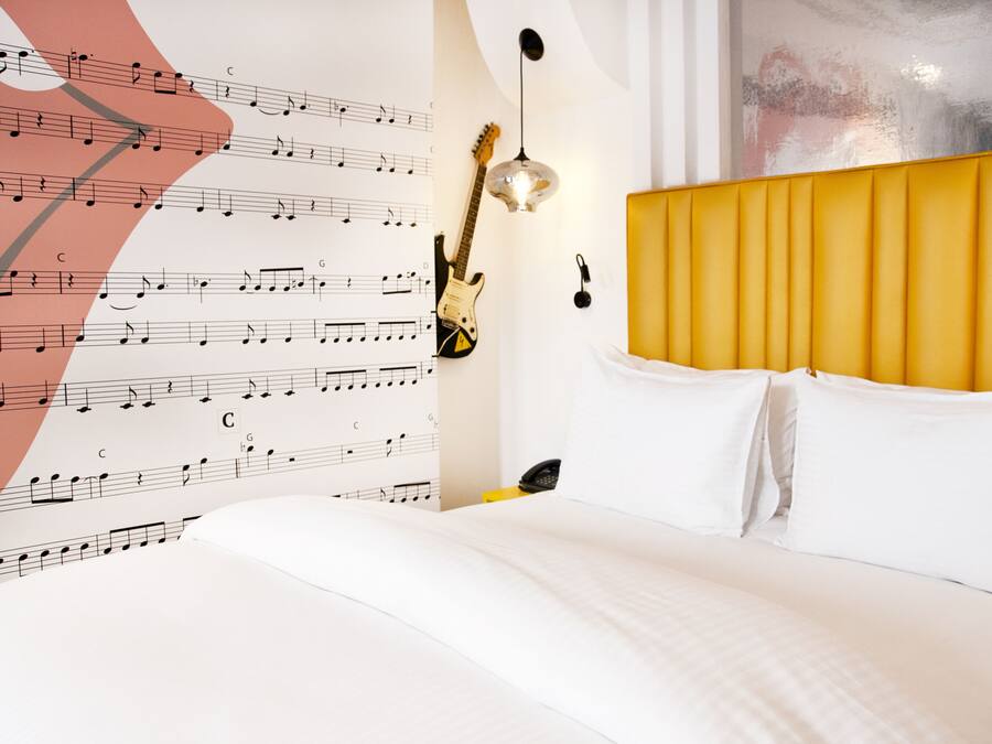 Habitación de hotel con una cama, una guitarra y una pared decorada con notas musicales.