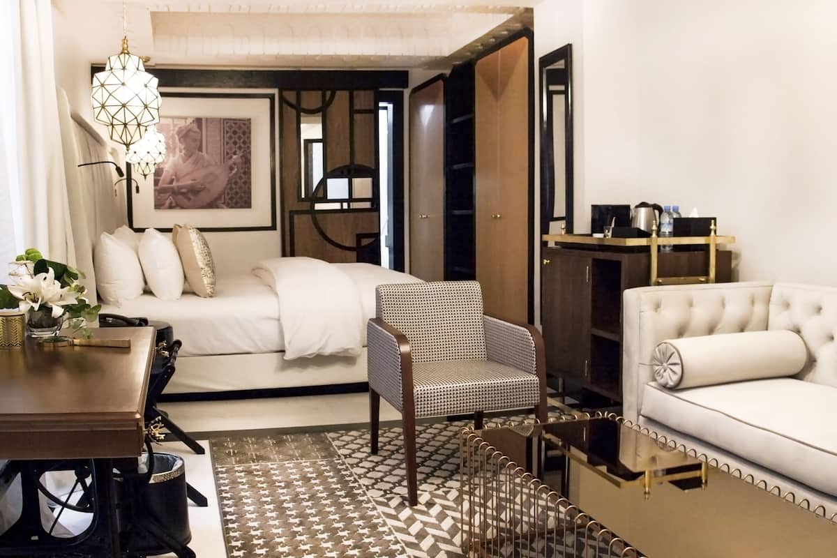 A modern hotel room with a bed, a sofa, a chair, a desk, and a coffee table.