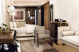 Habitación de hotel moderna con cama, sofá, sillón, escritorio y mesa de centro.