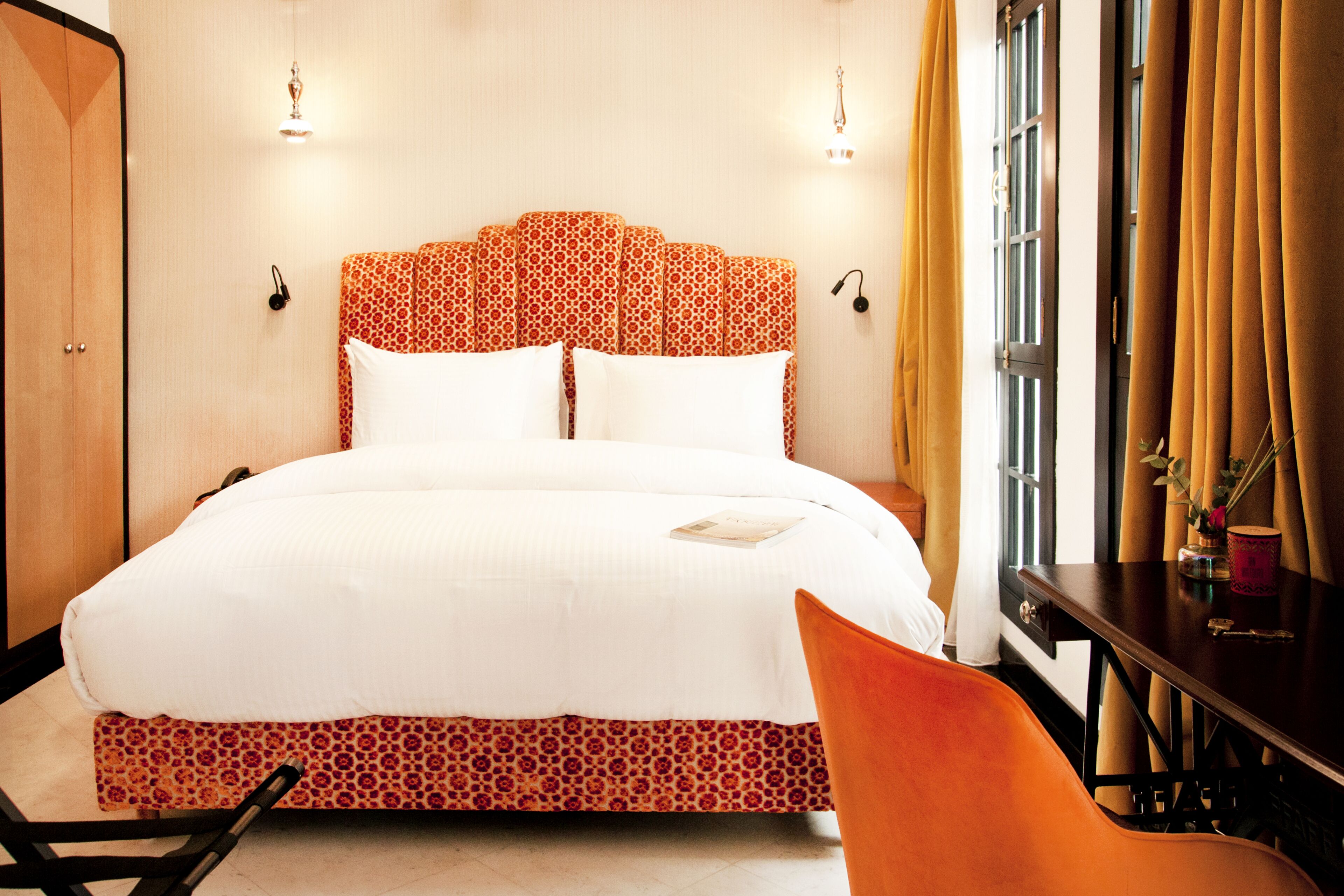A hotel room with a large bed, a wooden wardrobe, a desk, and a chair.