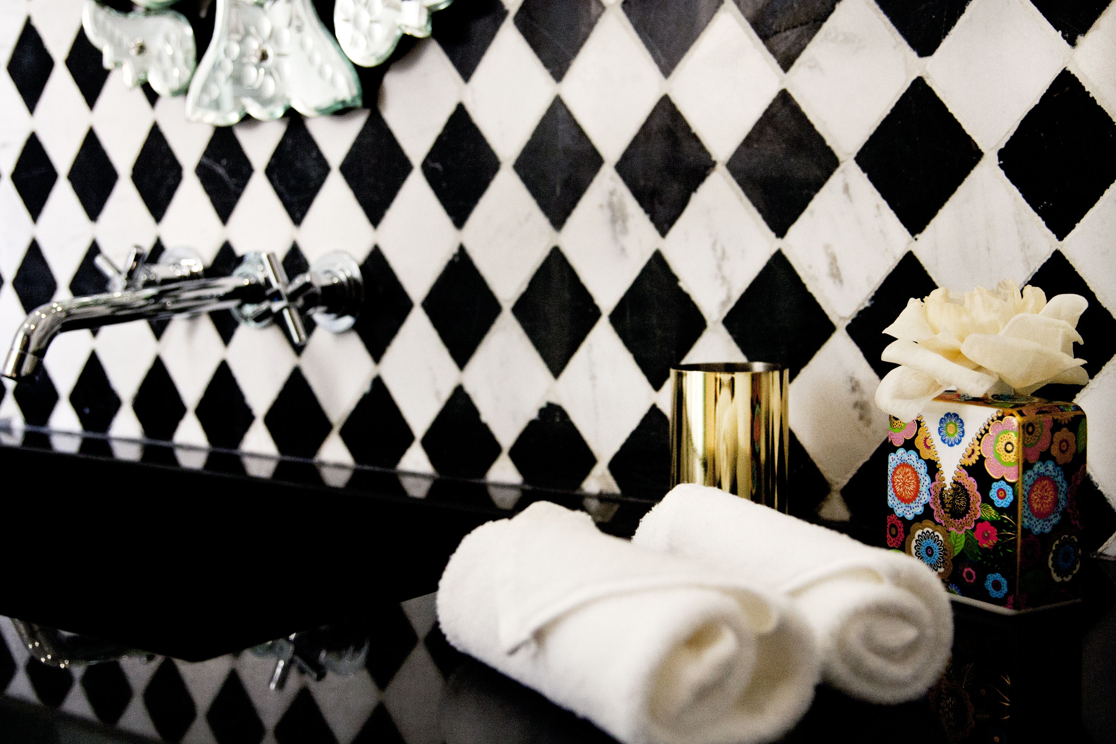 A bathroom with a black and white diamond-patterned tile wall, a black sink, and a decorative box with colorful floral patterns.