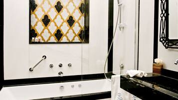 A bathroom with a black and white tiled wall, a glass shower enclosure, a white bathtub, and a black countertop with a towel.