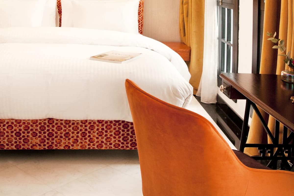 A hotel room with a large bed, a wooden nightstand, a chair, and a window with curtains.