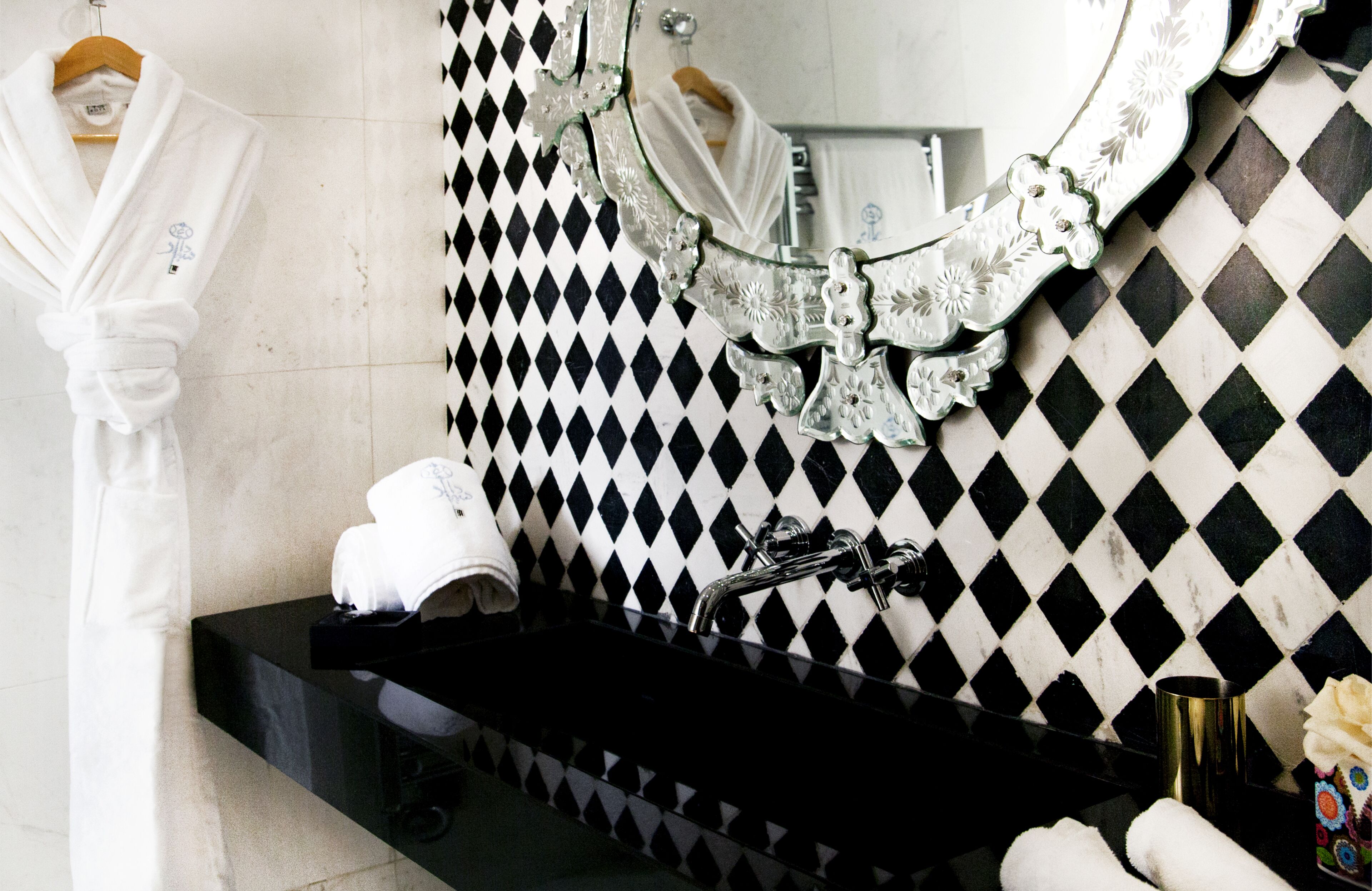 Un baño con pared de baldosas blancas y negras en damero, un lavamanos negro y un espejo con marco decorativo.
