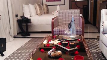 A modern living room with a sofa, a patterned armchair, a coffee table with a tray of pastries, and a red mug.