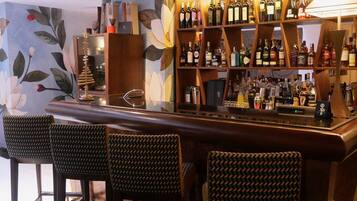 A bar area with a wooden bar counter, multiple shelves of liquor bottles, and three patterned bar stools.