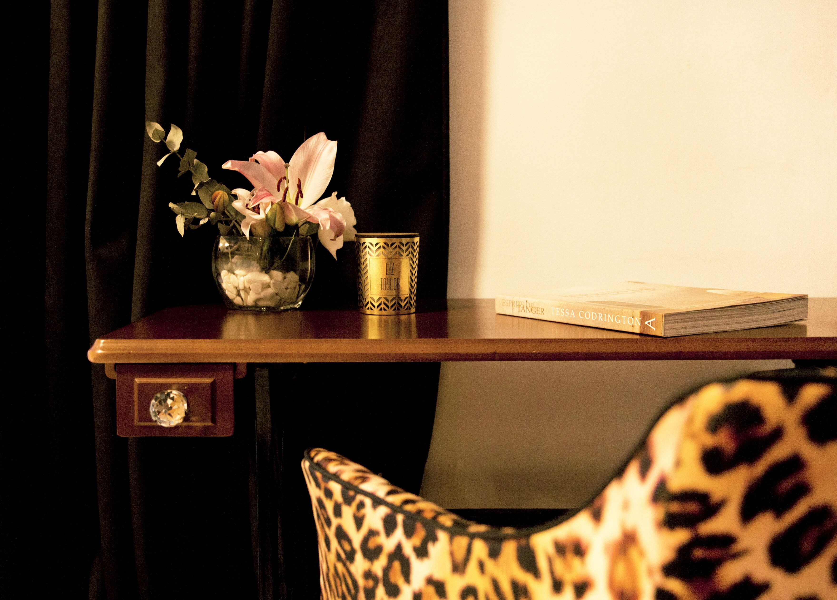 A wooden table with a vase of flowers, a candle, and a book.