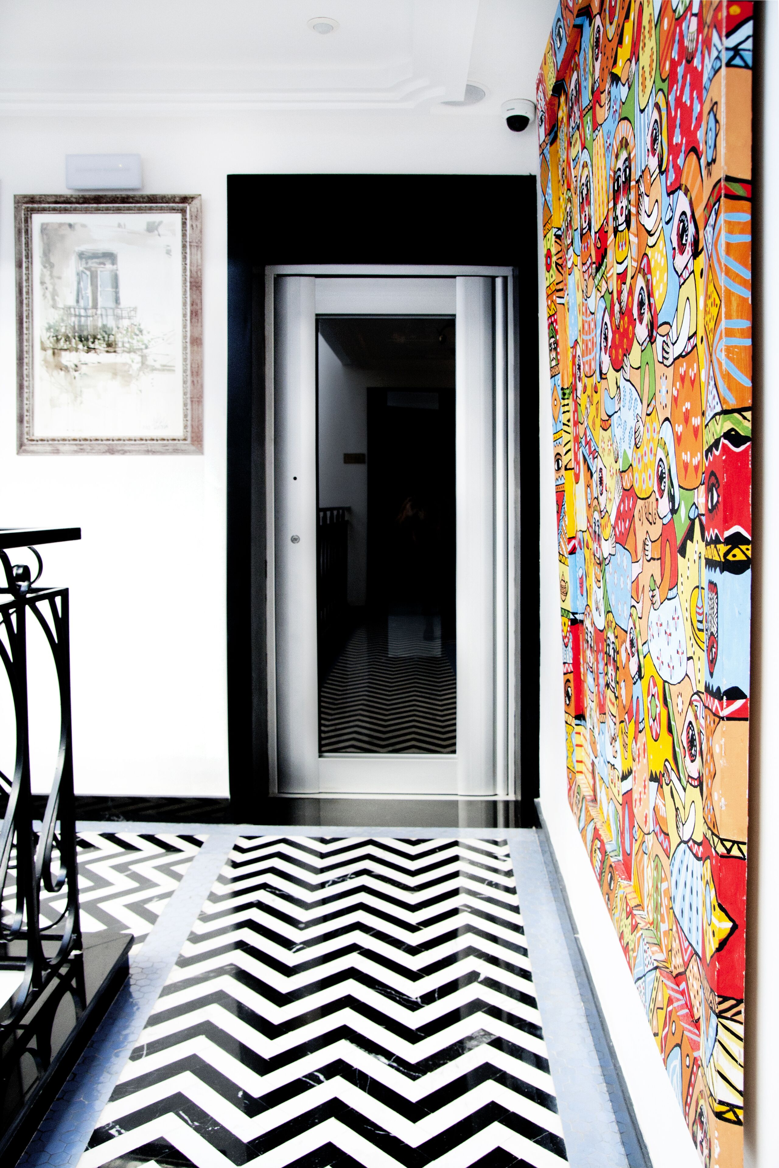 Un pasillo con suelo a cuadros blancos y negros, un mural colorido a la derecha y un cuadro enmarcado a la izquierda.