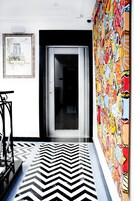 Un pasillo con suelo a cuadros blancos y negros, un mural colorido a la derecha y un cuadro enmarcado a la izquierda.