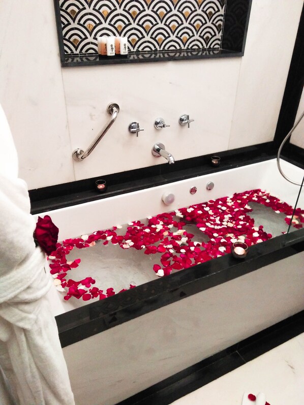 A bathtub filled with rose petals, a handrail, and a small candle.