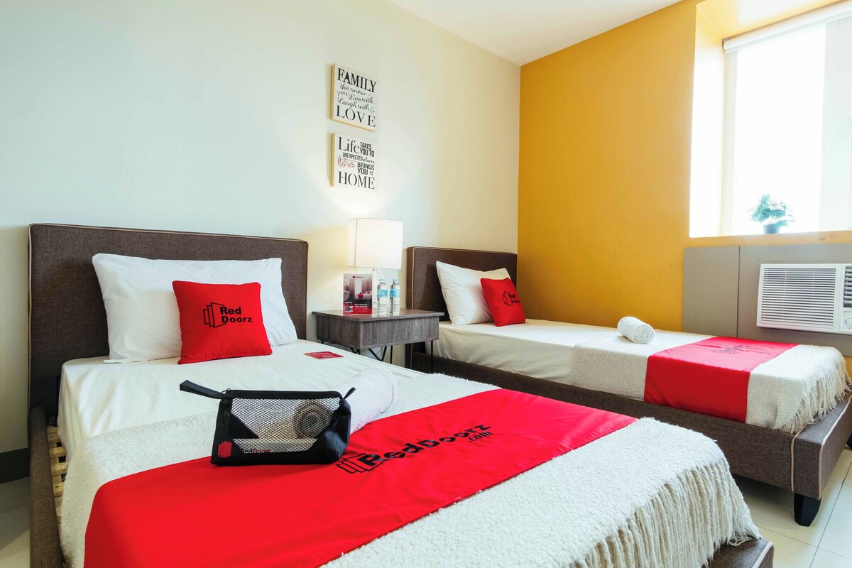 A hotel room with two beds, each with a red and white bedspread, a small bedside table with a lamp, and a wall with motivational quotes.