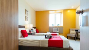 A hotel room with two beds, a desk, a chair, a window with blinds, and a wall-mounted air conditioner. - RedDoorz Plus @ Kamuning Quezon City (Quezon City)