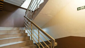 A staircase with a metal handrail and a green emergency exit sign. - RedDoorz Plus @ Kamuning Quezon City (Quezon City)