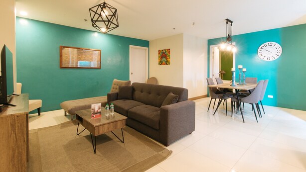 A modern living room with a sofa, coffee table, and a dining area with a table and chairs. - RedDoorz Plus @ Kamuning Quezon City (Quezon City)