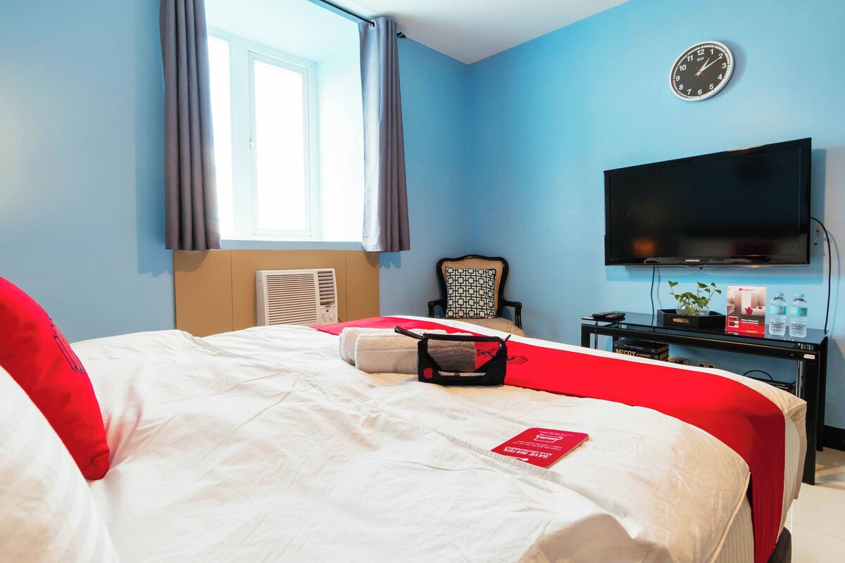 A hotel room with a bed, a television, a clock, and a window with curtains.